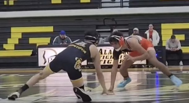 A teen boy in an orange wrestling uniform takes a low position as he eyes an opponent in black and gold.