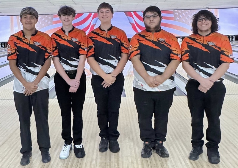 A group of five male bowlers poses for a photo in front of a bowling lane.