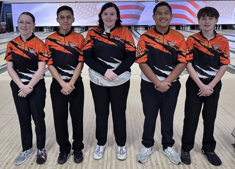 Two female and three male bowlers pose for a photo in front of a bowling lane.