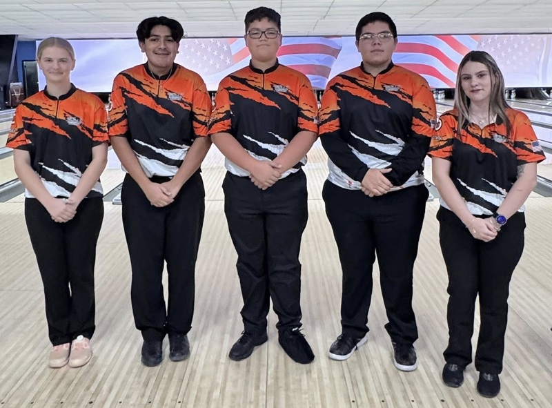 Two female and three male bowlers pose for a photo in front of a bowling lane.