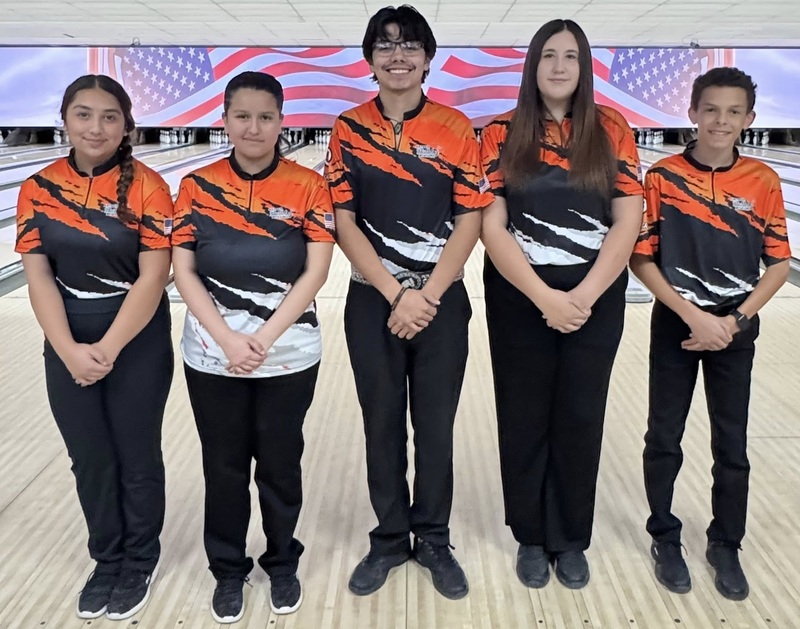 Three female and two male bowlers pose for a photo in front of a bowling lane.