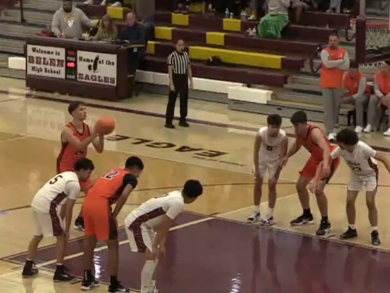 A teen boy in an orange and black basketball uniform stands at the free-throw line in preparation to shoot as teammates and opponents in white get in position to rebound.