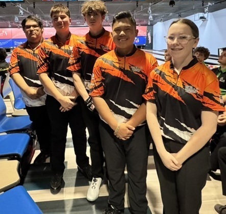 One female and four male teens in orange, black and white bowling shirts pose for a photo.