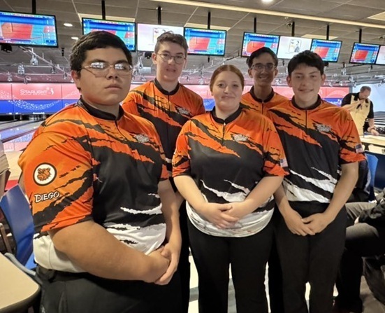 One female and four male teens in orange, black and white bowling shirts pose for a photo.