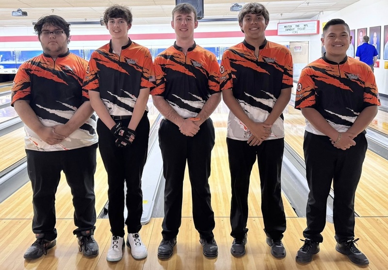 Five male teens in orange, black and white bowling shirts pose for a photo.