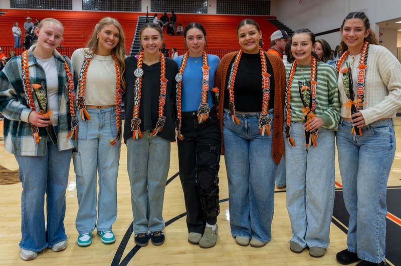 Seven female teens stand in a line as they smile for the camera.