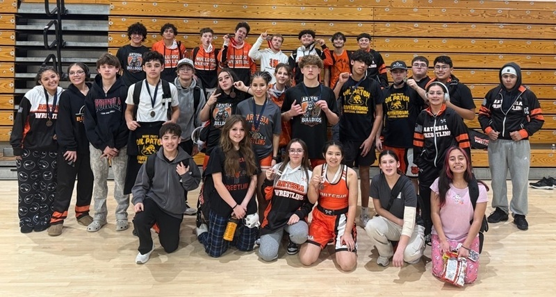 A large group of male and female teens, some wearing medals around their necks, pose for a photo in a gymnasium.