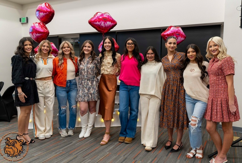 Ten teen girls wearing a variety of casual fashion outfits pose for a photo in front of floating balloons shaped like lip prints.