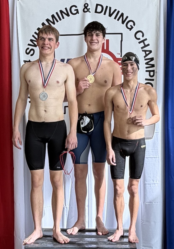 Three teen boys in black swim trunks pose for a photo atop a podium wearing, from left, silver, gold and bronze medals around their necks.