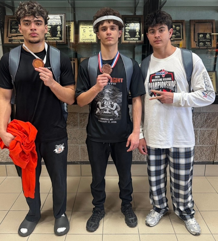 Three teen boys in t-shirts and loose pants pose for a photo. Two show medals hanging around their necks and one flashes a peace sign.