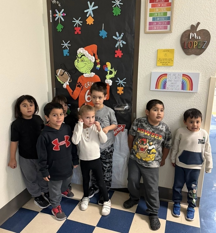A small group of male and female children pose for a photo in front of a classroom door that features an image of the Grinch in an Artesia Bulldog football jersey.