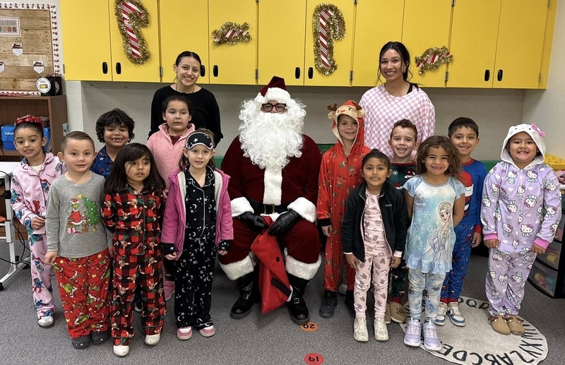A group of male and female children wearing pajamas pose for a photo around a person dressed as Santa Claus.