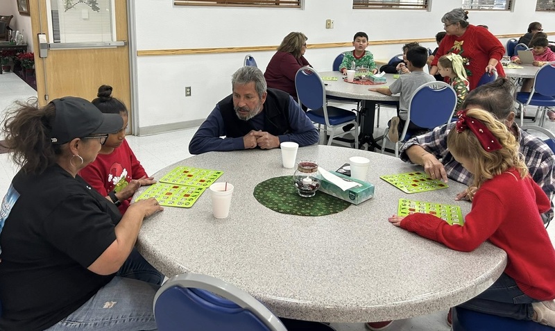 Children and senior citizens seated at a round table look at their green Bingo cards.