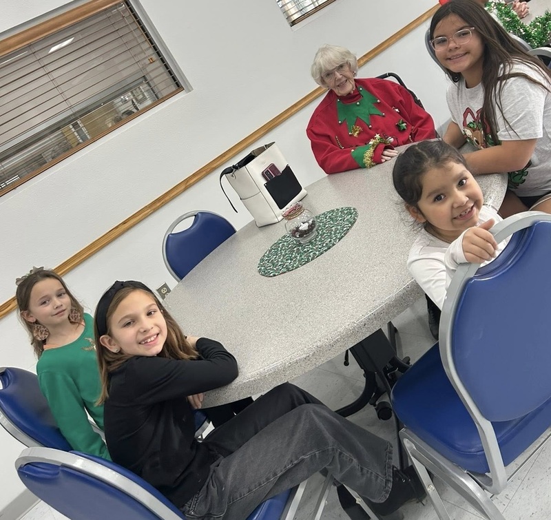 Four female children and an elderly woman pose for a photo while seated around a round table.