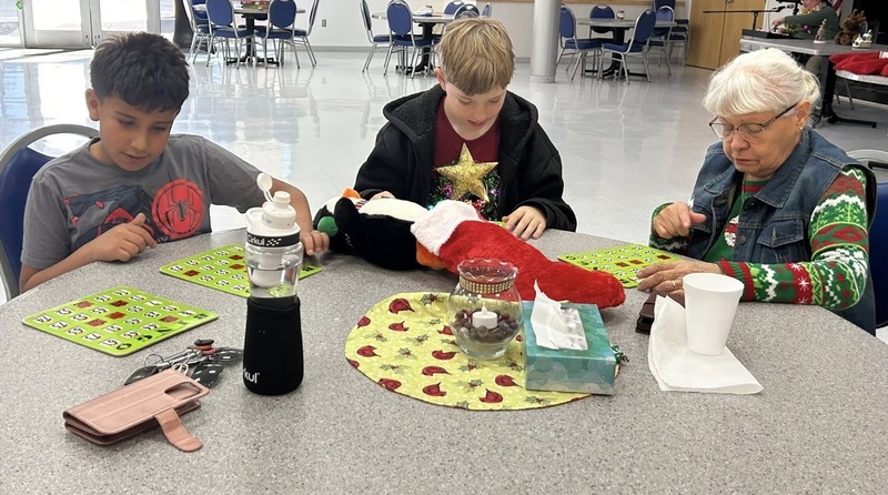 Two young boys play Bingo with an elderly woman.