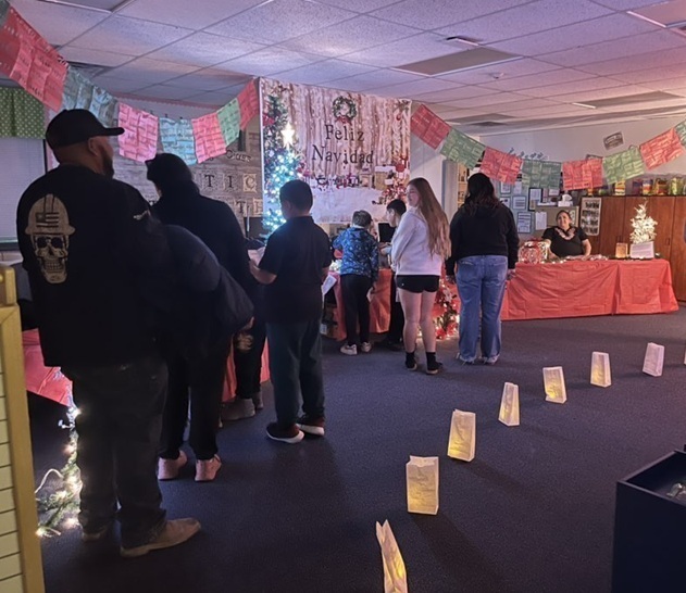 Children and adults make their way along a row of luminarias into a classroom decorated like Christmas in Mexico.