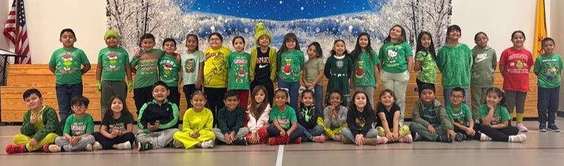A large group of children, all dressed in green and/or Grinch-related attire, poses for a photo.