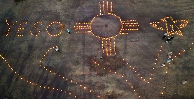 As soon from above, luminaries spell out the word "Yeso" and depict a Zia sun symbol and a thunderbird.