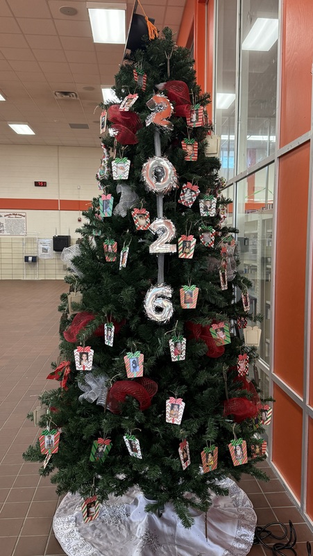 A Christmas tree in a school commons area is decorated with the numbers "2026" and baby photos of senior students.