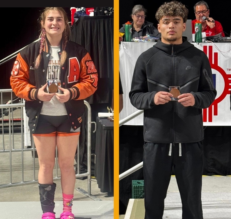 A teen girl in an orange and black letter jacket and shorts with a brace around one ankle and a teen boy all in black pose for photos holding medals.