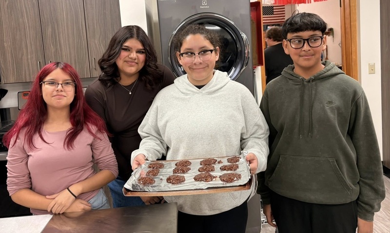 Two teen girls and two teen boys pose for the camera. One boy holds a tray of chocolate cookies.