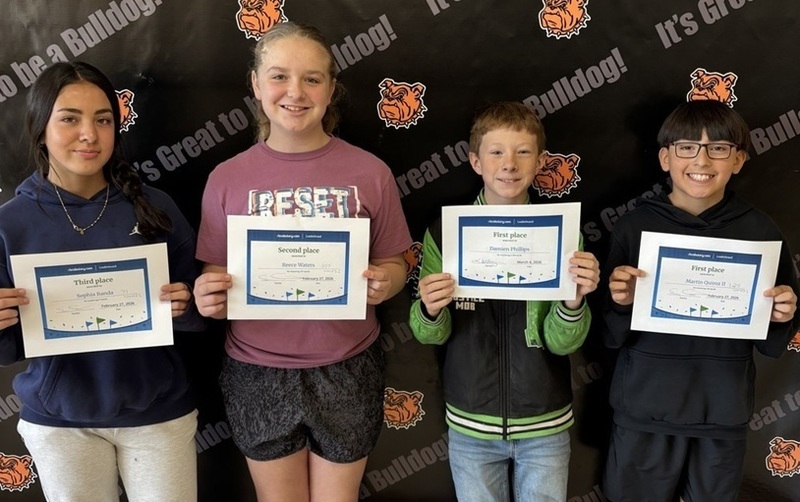 Two preteen girls and two preteen boys smile for the camera while holding certificates.