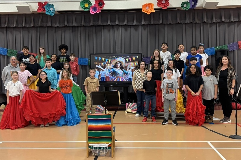 Young students stand on either side of a TV featuring an image of a Spanish dancer. Some of the students are dressed in flamenco attire.