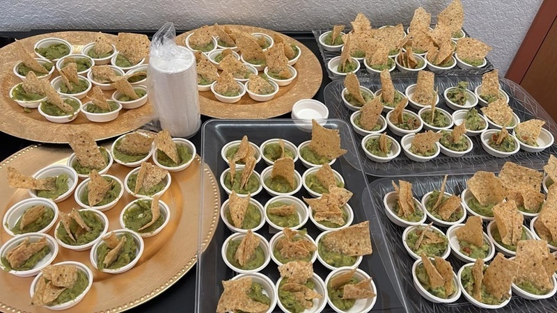 Small cups of guacamole, each with a tortilla chip protruding from them, sit on trays on a table.