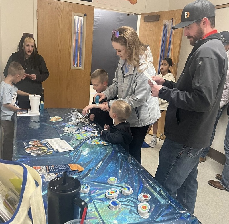 A man, a woman and a male child stand at a table examining the space-themed stickers laid out on it.