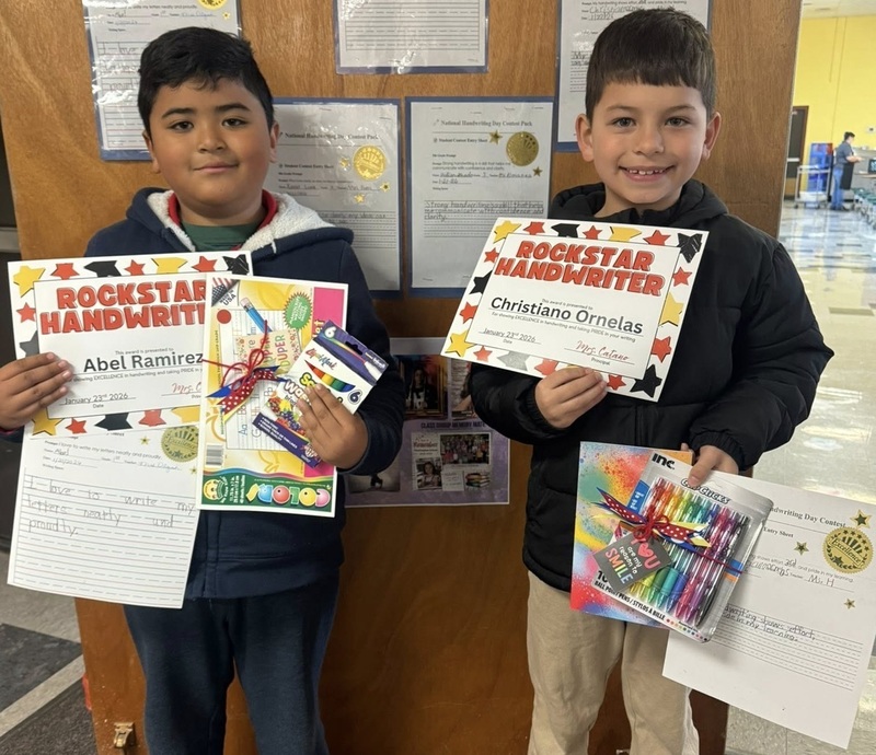 Two yoiung boys smile for the camera while holding certificates, pens, pencils, and workbooks.
