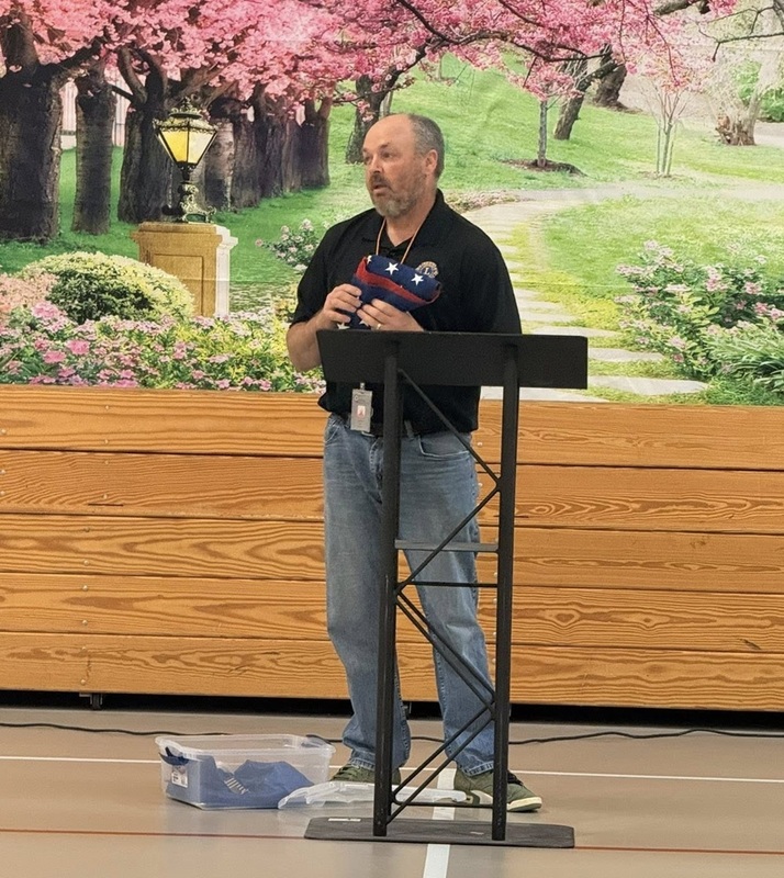 A man is seen standing at a podium in a school gym.