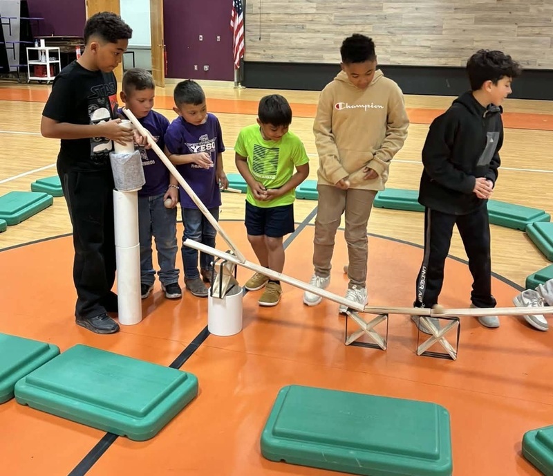 Six young boys stand in a row behind an experiment built from paper tubes and plastic tub lids.