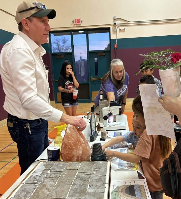 Children stand at a science experiment station featuring a large rock of pink salt as a man stands behind it.