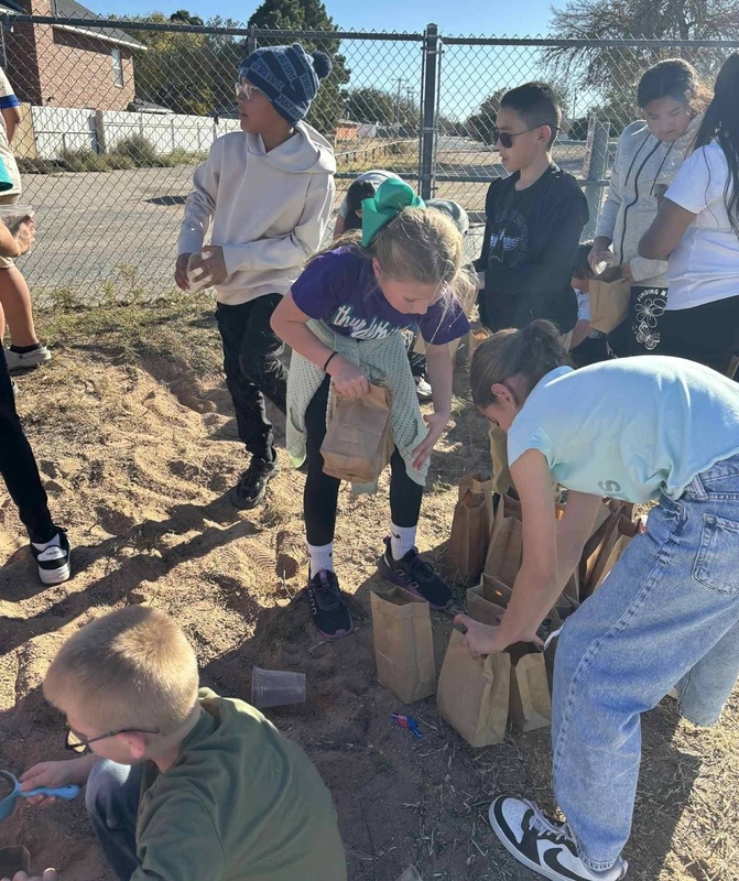 Children on a school playground work to fill paper bags with sand.