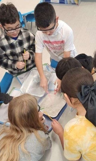 A group of children examines sand in a tin pan.