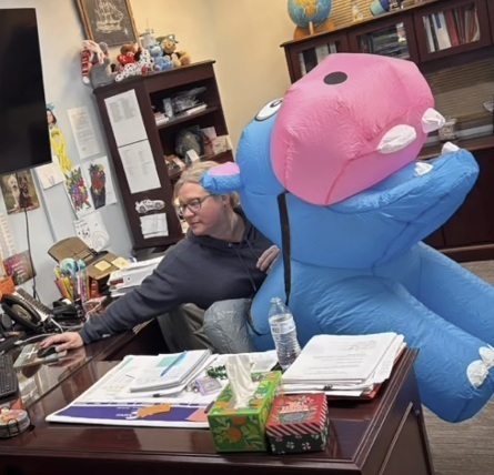A woman sits at a desk and attempts to work on a computer while dressed as an inflatable hippo.
