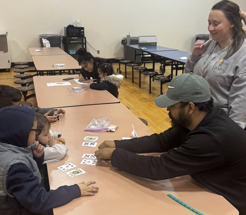 Two young children watch as a man presents them with playing cards.