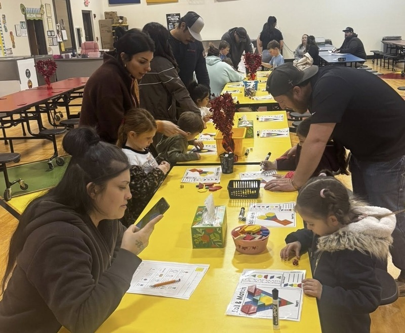 A small child looks at a worksheet featuring a colorful heart as a woman seated across from her looks on.