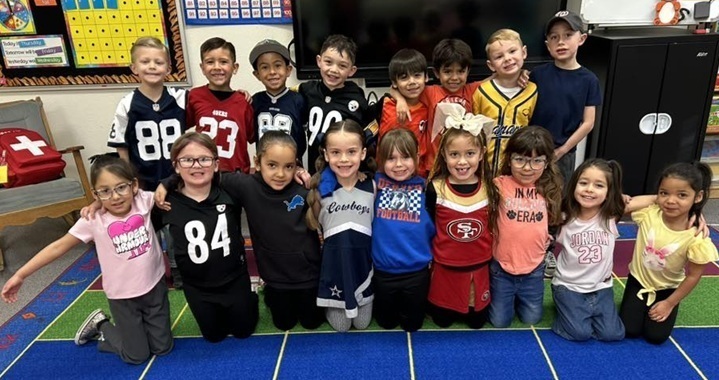 A group of smile children pose for a photo. Many of them wear numbered jerseys and team attire.