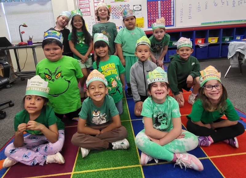 A group of children in green clothing smiles for the camera.