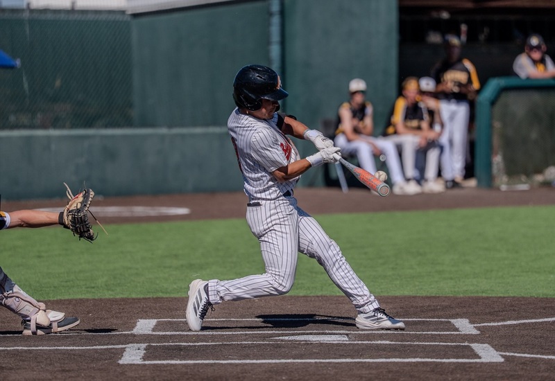 A teen boy in a grey and orange baseball uniform hits the ball with the bat.