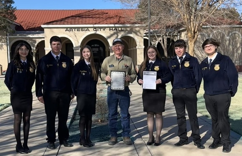 Three teen girls and three teen boys in blue FFA jackets pose for a photo surrounding a man who is holding a certificate.
