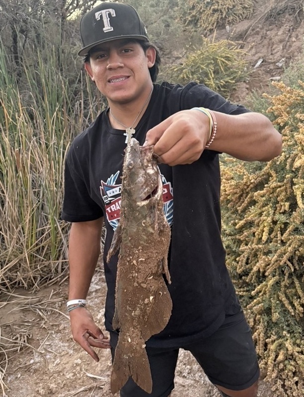 A teen boy dressed in black holds up a fish.