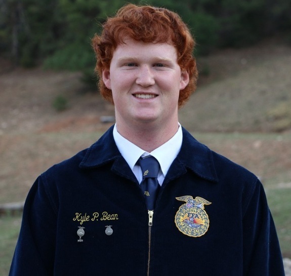 A teen boy with red hair poses for a photo wearing an FFA jacket.