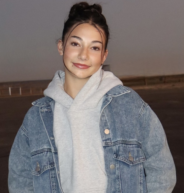 A teen girl poses for a photo wearing a sweatshirt and a jean jacket.