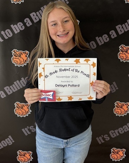A teen girl in a black shirt and jeans holds a certificate that reads "Seventh-Grade Student of the Month".