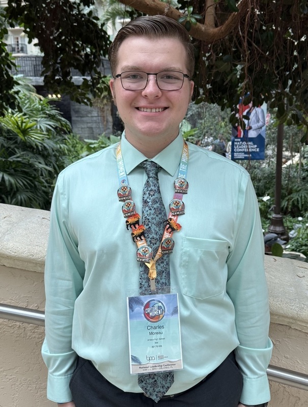 A teen boy in a light-green dress shirt wearing a lanyard around his neck poses for a photo.