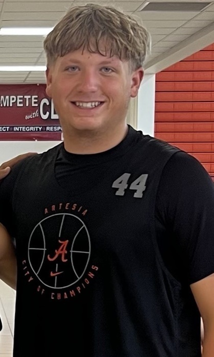 A teen boy in a black t-shirt with a basketball on the front poses for a photo.