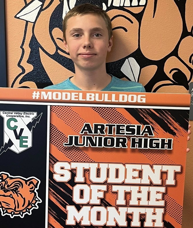 A teen boy in a light-green shirt holds a sign reading "Student of the Month".