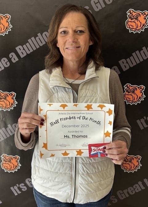 A female teacher in a long-sleeved mauve shirt and cream-colored vest holds a certificate reading "Teacher of the Month".
